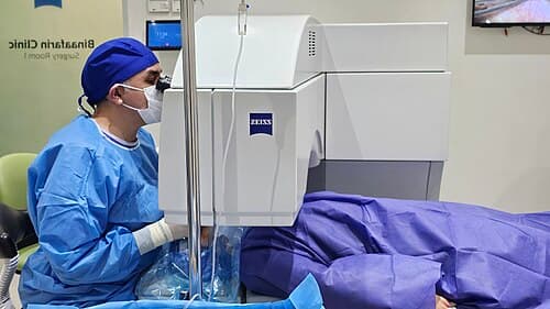 An eye surgeon operating a refractive laser platform on a draped patient in a clinic laser suite.