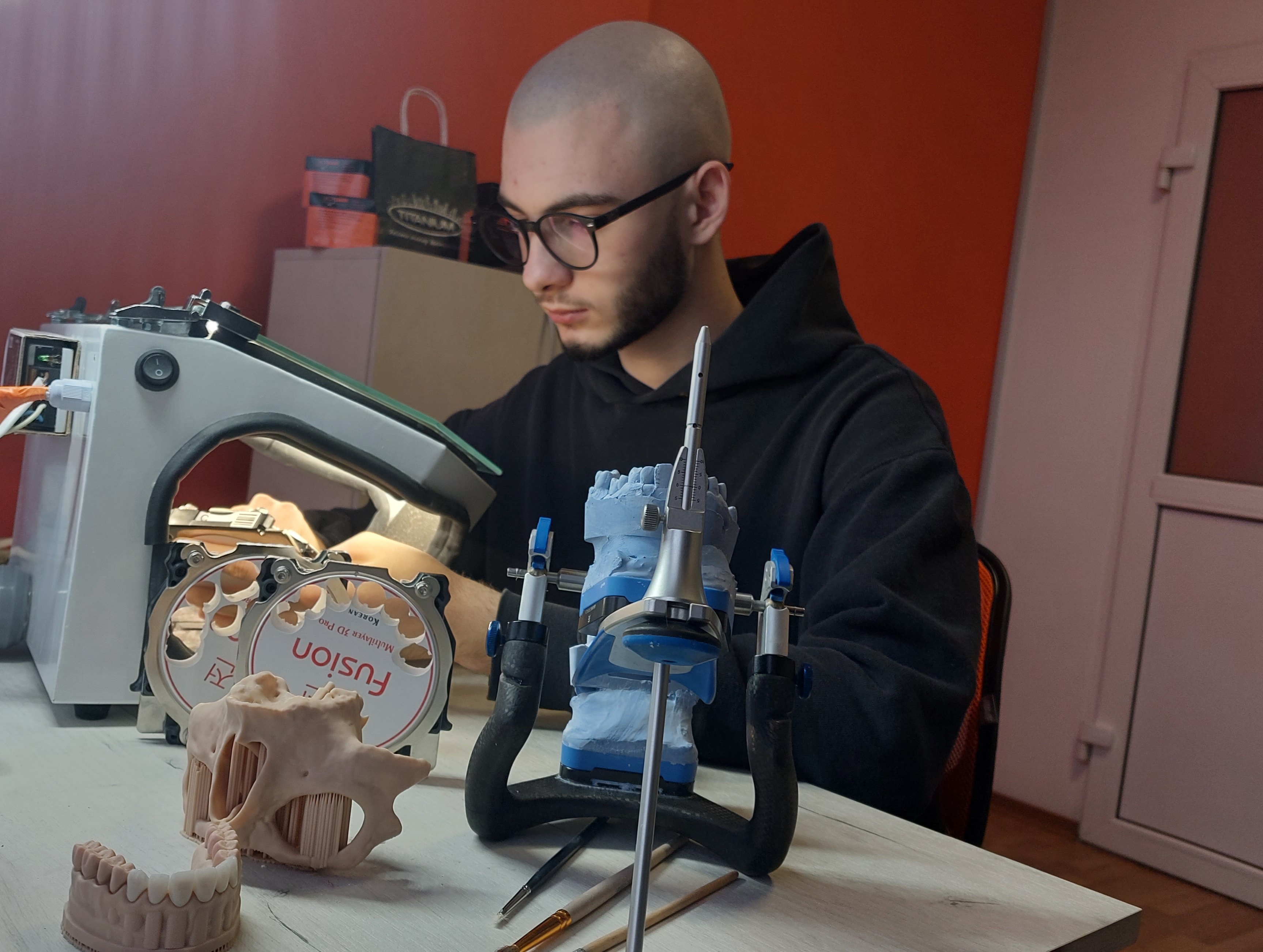 A dental technician at a laboratory bench working on plaster tooth models mounted in an articulator.